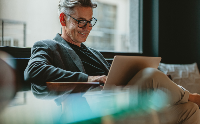 A man sitting a sofa and smiling to a laptop.