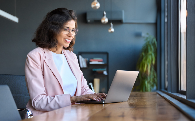 Smiling woman in glasses working on a laptop.