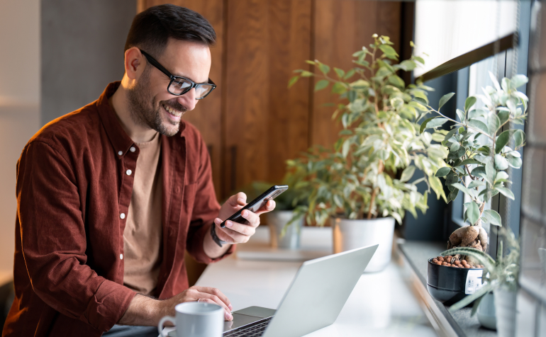 Smiling man using smartphone and laptop.