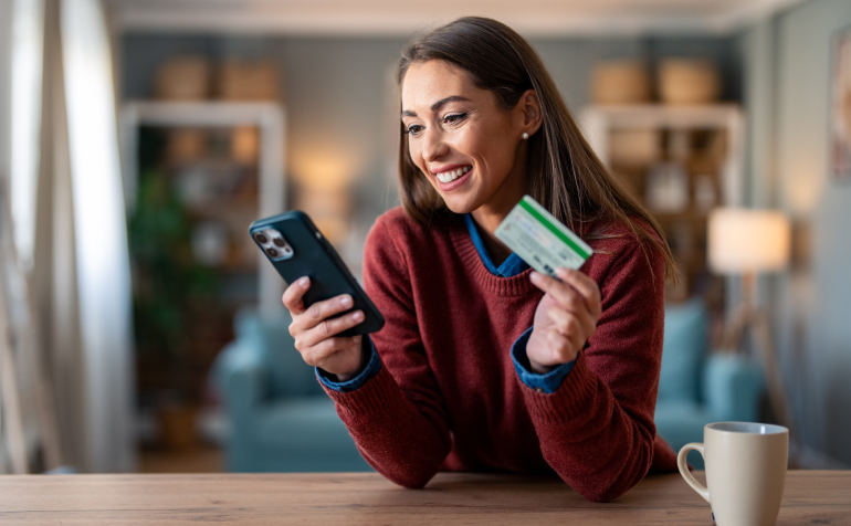 Happy woman holding credit card and smiling to a smartphone.