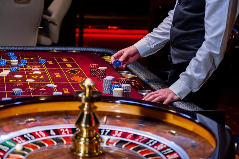A professional croupier stands behind a roulette table, handling chips and overseeing gameplay.