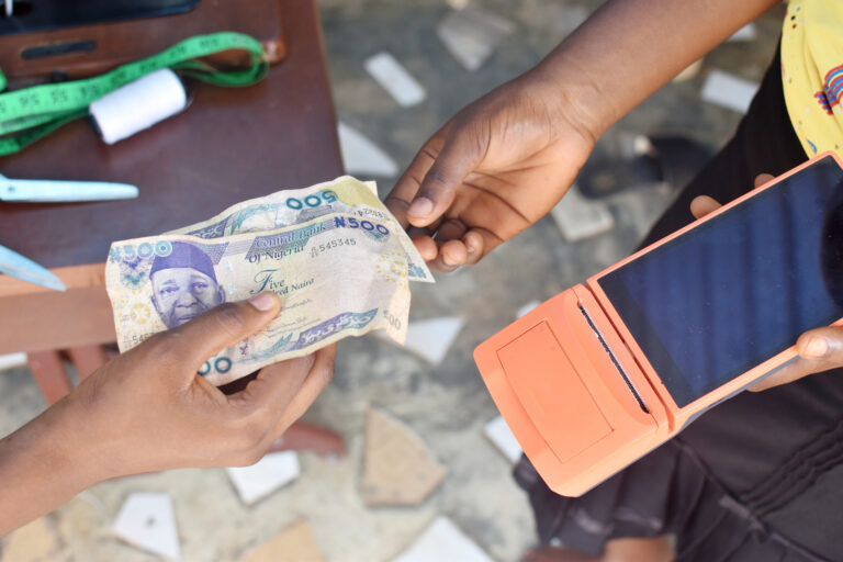 Hands exchanging 500 Nigerian naira over an orange mobile payment, symbolizing mobile-pay innovation in Africa.