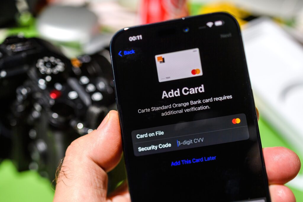 A hand holding a smart phone showing digital wallet screen prompting to add Mastercard by entering the 3-digit CVV for verification.